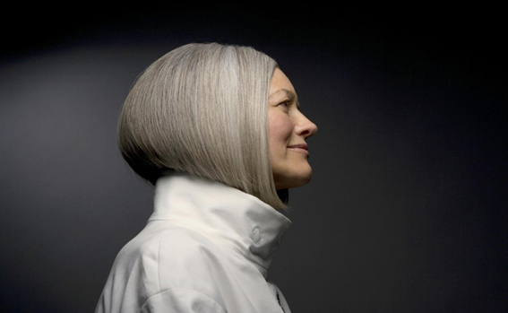 A woman with gray hair wearing a white jacket. Image depicts the natural process of hair turning gray over time